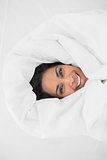 Cheerful woman lying under cover on her bed