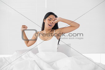 Cute dark haired woman stretching out while sitting on her bed