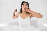 Cute young woman yawning while sitting on her bed