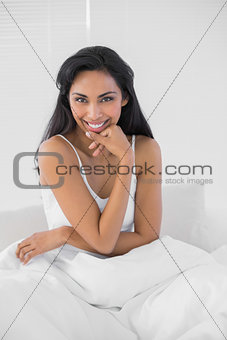 Lovely dark haired woman posing while sitting on her bed