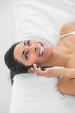 Natural laughing woman phoning with smartphone lying on bed