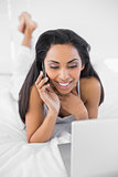Happy natural woman phoning while using her notebook