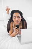 Cute natural woman using her smartphone lying on bed