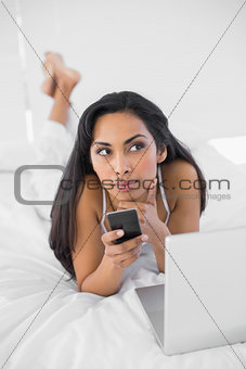 Natural thinking woman holding her smartphone