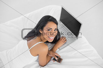 Happy smiling woman lying on her bed holding her phone