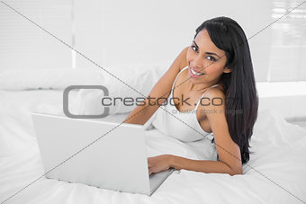 Relaxing natural woman lying on her bed using her notebook