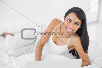 Sweet natural woman using her laptop lying on her bed
