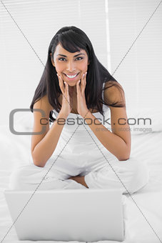 Lovely smiling woman sitting on bed in front of her notebook