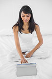 Beautiful serious woman using her tablet sitting on bed