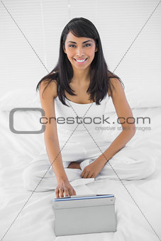 Smiling young woman using her tablet sitting on bed