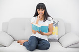 Calm dark haired woman reading a book sitting on couch