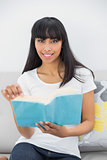Attractive dark haired woman holding a book while sitting on couch