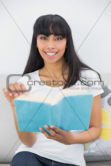 Beautiful dark haired woman holding a book while smiling at camera