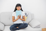Thoughtful young woman holding a book sitting on couch