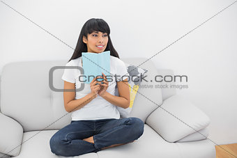 Thoughtful young woman holding a book sitting on couch