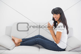Gleeful young woman holding a cup sitting on couch