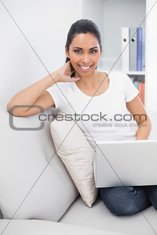 Gleeful young woman using her notebook sitting on couch