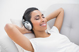 Cute smiling woman lying on couch while listening to music