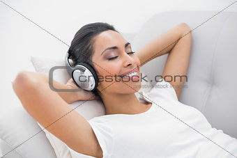 Cute smiling woman lying on couch while listening to music