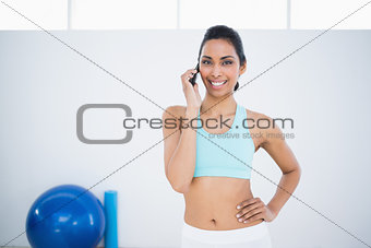 Gleeful sporty woman phoning while standing in fitness hall