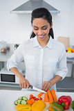 Cute smiling woman cutting vegetables standing in kitchen
