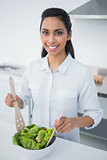 Attractive black haired woman preparing salad in kitchen