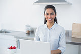Content woman using her notebook standing in bright kitchen