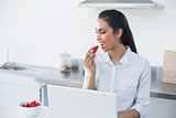 Peaceful dark haired woman eating strawberry