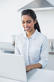 Gleeful woman typing on her laptop standing in bright kitchen