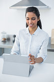 Lovely smiling woman using her tablet standing in bright kitchen