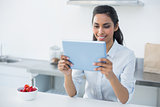 Smiling woman holding her tablet standing in bright kitchen