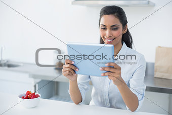 Smiling woman holding her tablet standing in bright kitchen