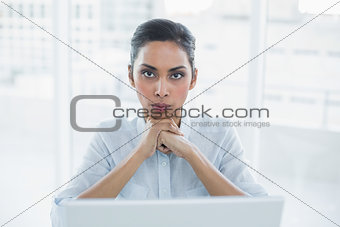 Stern businesswoman sitting at her desk looking at camera