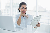 Cute smiling businesswoman holding newspaper sitting at her desk