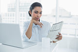Serious businesswoman reading newspaper sitting at her desk