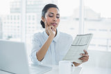 Focused businesswoman reading newspaper sitting at her desk