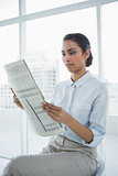 Softly smiling chic businesswoman reading newspaper