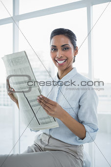 Gleeful chic businesswoman holding newspaper smiling at camera