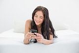 Smiling woman looking at mobile phone in bed
