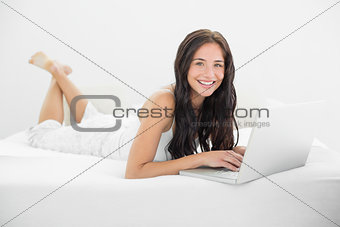 Portrait of a smiling casual woman with laptop in bed