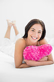 Smiling woman lying with heart shaped pillow in bed