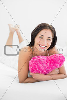 Smiling woman lying with heart shaped pillow in bed