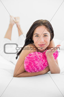Woman with heart shaped pillow blowing kiss in bed