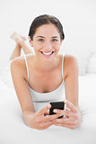 Portrait of a smiling woman with mobile phone in bed
