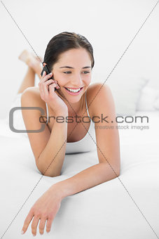Smiling woman using mobile phone in bed