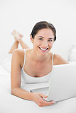 Portrait of a smiling casual woman using laptop in bed
