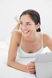 Smiling casual woman with tablet PC looks away in bed