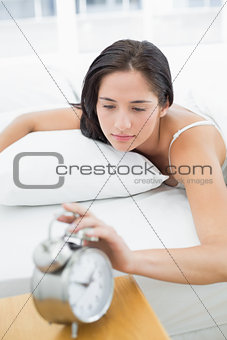 Woman in bed extending hand to alarm clock