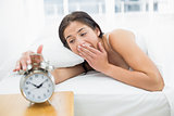 Woman yawning while extanding hand to alarm clock