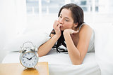 Thoughtful woman in bed with alarm clock in foreground